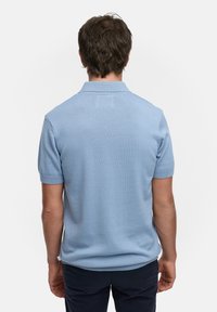Polo de manga corta azul claro, con cuello y puños acanalados, textura suave, diseño ajustado, con la etiqueta visible en la parte posterior del cuello.