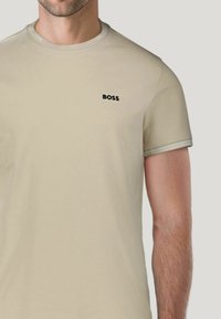 Beige short-sleeve t-shirt made of cotton, featuring a crew neck and black "BOSS" logo on the chest. Accents in a lighter beige shade.
