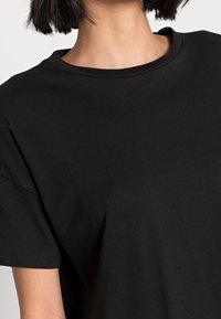 Svart bomullströja med rundad halsringning, korta ärmar och en mjuk textur. Inga synliga mönster eller dekorationer.