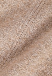 Beige tyg med en mjuk, strukturerad yta som har subtila färgvariationer och synliga sömlinjer.