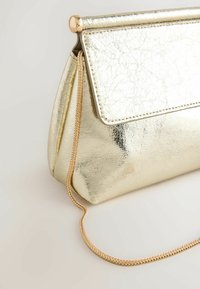 Petit sac à main métallique doré avec fermeture à rabat et fine bandoulière tressée, sur un fond clair.