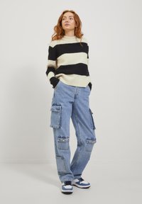 Schwarz-cream gestreifter Pullover, lockere blaue Cargo-Hose mit Fronttaschen und sportlichen blau-weißen Sneakers. Lässiger Stil.