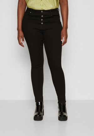 Jeans negros ajustados de mezclilla con cintura alta y cierre de cinco botones. Llevados con una camisa a rayas verdes y botas de plataforma negras brillantes.