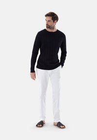 Marineblauer Kabelstrickpullover, weiße Hose und schwarze Rutschsandalen. Verfügt über ein strukturiertes Design mit gerippten Bündchen und Rundhalsausschnitt.