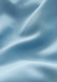 Tissu lisse bleu clair avec une texture légèrement brillante, présentant des drapés doux et des plis subtils, mettant en valeur sa nature souple et légère.
