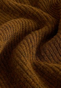 Brauner texturierter Stoff mit geripptem Design, der warme Brauntöne und Orangetöne präsentiert und ein sanftes, gemütliches Erscheinungsbild schafft.