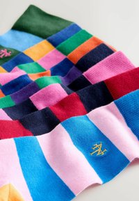 Chaussettes rayées colorées dans divers motifs disposées côte à côte, avec des bleus vifs, des roses, des verts, des rouges et de petits logos dorés brodés.