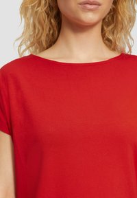 Rotes kurzärmeliges Oberteil aus weichem Stoff mit Rundhalsausschnitt, das eine glatte Textur und ein einfaches Design ohne Muster oder Akzente aufweist.