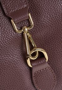 Cinghia di una borsa a tracolla in pelle marrone con superficie testurizzata, dotata di accessori in oro e di una chiusura per il fissaggio.