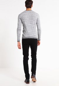 Šedý pletený svetr s kulatým výstřihem, fitted rukávy a žebrovaným lemem, zkombinovaný s černými slim-fit kalhotami a černými botami.