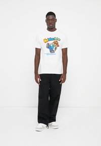 White t-shirt with colorful graphic design featuring a character and text. Black cargo pants. White sneakers with gray accents.