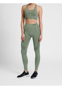 Soutien-gorge de sport vert olive et leggings taille haute assortis en tissu texturé avec des accents perforés. Chaussures de sport noires.