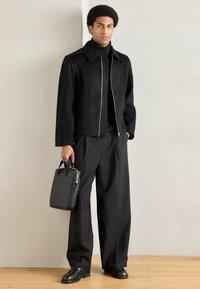 Crna jakna na patent s ovratnikom, uz to crni rolka, široke crne hlače i mala crna torbica. Glatka tekstura.