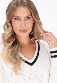 Maglione bianco lavorato a maglia con un motivo texturizzato, scollo a V e dettagli neri a strisce su collo e polsini. Tessuto liscio e leggero.