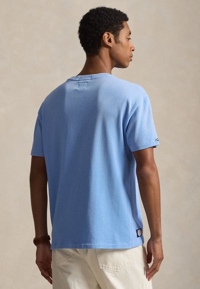 Tricou albastru deschis cu dungi, mâneci scurte, tiv drept și accent de logo aproape de bază. Confecționat din bumbac moale și texturat.