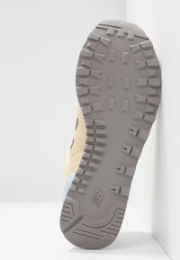 Sko sål med en gummigrå bund med mønstrede grebsmønstre; overdel i beige ruskind med hvide og lyseblå accenter.