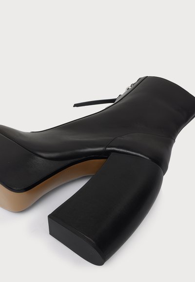 Botte noire à talon haut, épais et carré, avec fermeture éclair sur le côté intérieur, présentée sur fond blanc uni.
