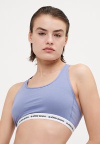 Ljusblå sportbh med en slät yta, med ett vitt band där "BJÖRN BORG" är tryckt i svart. Racerback-design, minimalistisk stil.