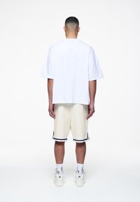 Biała, oversize'owa koszulka z krótkim rękawem, zestawiona z jasnobeżowymi szortami z czarnymi akcentami oraz białymi trampkami z detalami logo.