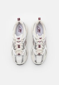 Baskets en mailles blanches et argentées avec des accents rouges. Présente un bout arrondi, des panneaux texturés et des lacets plats. Marque visible sur la languette.