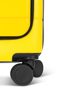 Gelber Hartschalenkoffer mit einem schwarzen Reißverschluss, glatter Textur und vier schwarzen Rollen für Mobilität. Abgerundete Ecken und elegantes Design.