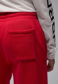 Punased dressipüksid on valmistatud tekstuurse kangaga, millel on elastne vöökoht ja tagatasku. Valge pika varrukaga särk on osaliselt nähtav.