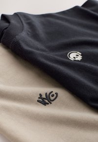 Due felpe piegate, una nera con un logo di teschio bianco con cuffie e una beige con logo testuale nero NYC.