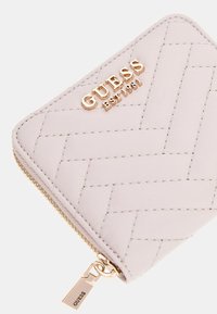 Portefeuille rose clair en matériau synthétique texturé, arborant un motif en chevrons et des accessoires en métal doré avec une fermeture éclair.