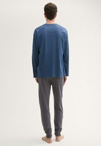 Une chemise bleue à manches longues associée à un pantalon de pyjama gris, tous deux fabriqués dans un tissu doux. Le pantalon a des poignets élastiques et une coupe décontractée.