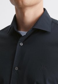 Donkerblauwe overhemdd met een klassieke kraag, twee knopen en een subtiel geborduurd logo op de borst. Glad textiel.