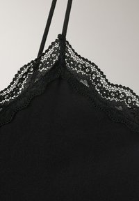 Haut caraco noir avec fines bretelles et un délicat galon de dentelle florale le long de l'encolure sur un fond uni.