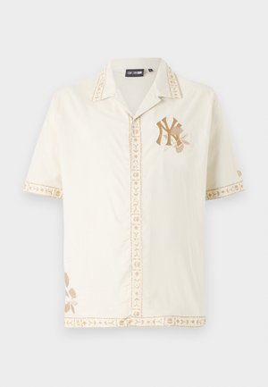 Korte mouwen crèmekleurig shirt met lichtbruine geborduurde bloemenaccenten en een logo. Kenmerkt zich door een kraag en decoratieve stiksels.