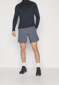 Svart långärmad zip-up tröja, grå shorts och svarta sportskor med orange detaljer. Har en snygg, kroppsnära design och ett ventilerande material.