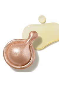 Rosa guldolja i kapslar med en glänsande yta, tillsammans med gula och genomskinliga vätskedroppar på en vit bakgrund.