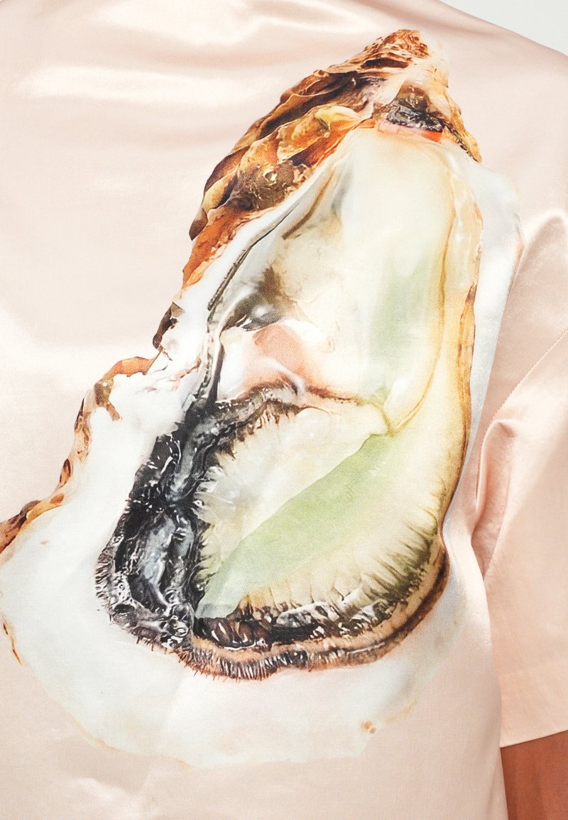 Satinhemd in sanftem Rosa mit einem großen, detaillierten Austernmuster in grünen, schwarzen und braunen Tönen, mit glatter Textur und starken Kontrasten.