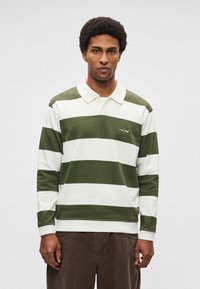 Roheline-valgete triipudega pikkade varrukatega polo särk krae ja logoga tikandiga; valmistatud pehmest kangast; lõdva istuvusega.