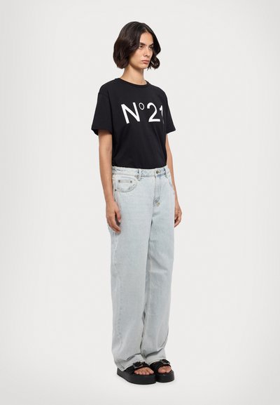 Zwarte t-shirt met opvallende witte "N°21" grafiek, gecombineerd met lichtblauwe wijde jeans en zwarte platform sandalen. Eenvoudig, casual ontwerp.