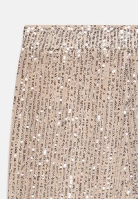 Legging beige avec des rayures verticales en sequins argentés sur un tissu doux et texturé. Taille élastique avec des accents brillants sur l'ensemble du design.