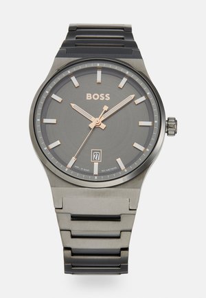 Analoguhr mit grauem Zifferblatt, roségoldenen Akzenten und einem Stahlgehäuse. Verfügt über ein schwarzes Metallarmband und eine Datumsanzeige an der 6-Uhr-Position.