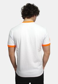 T-shirt bianca a maniche corte, con dettagli arancioni nei collari e nei polsini. Tessuto liscio, vestibilità casual.