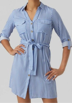 Blau-weiß gestreiftes Kleid mit Kragen, Knopfleiste, zwei Brusttaschen und Taillengürtel. Lange Ärmel, hochgekrempelt bis zu den Ellbogen.