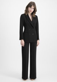 Black double-breasted blazer with notched lapels and front pockets, paired with matching wide-leg trousers. Smooth, tailored fabric.