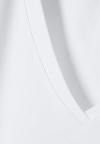 Tejido blanco y liso con un diseño de escote en V. Presenta costuras limpias y una textura suave, destacando un estilo minimalista.