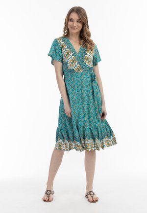 Rochie wrap turcoaz cu imprimeu floral, cu mâneci scurte, decolteu în V și tiv în mai multe straturi. Prezintă un print floral alb și portocaliu pe margini.