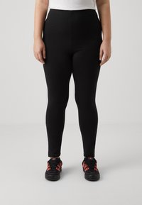 Black leggings made of stretchy material, featuring a high waist and a smooth texture. Paired with black and red athletic shoes.