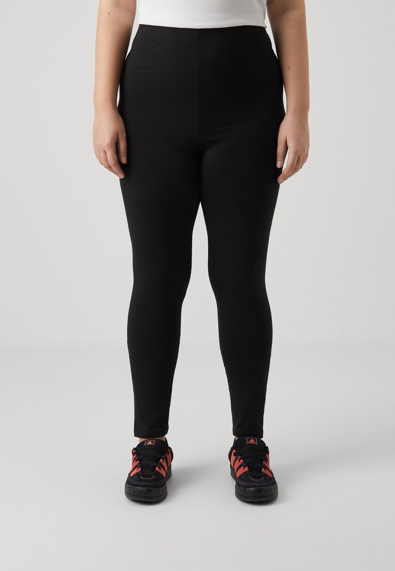Black leggings made of stretchy material, featuring a high waist and a smooth texture. Paired with black and red athletic shoes.