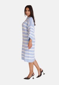 Strickkleid mit horizontalen hellblauen und weißen Streifen, mit hohem Kragen und Dreiviertelärmeln, kombiniert mit schwarzen Slingback-Highheels.
