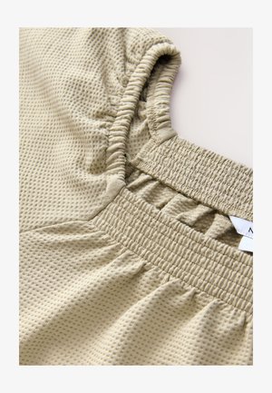 Svetlo béžový top s textúrovaným vzorom pripomínajúcim mriežku, elastickými manžetami a nazberaným pásom pre priliehavý strih.