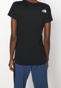 Svart bomullströja med rund hals, korta ärmar och en liten vit logotyp på den övre ryggen. Slät textur och vanlig passform.