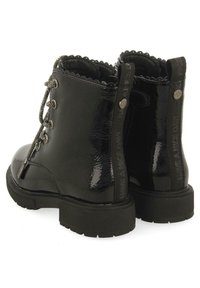 Botas de tobillo de charol negro con punta redondeada, cordones en la parte delantera, cuello decorativo con bordes ondulados, suela de goma texturizada y marca en el talón.